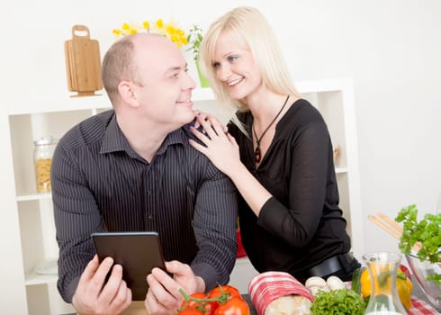 Affectionate attractive middle-aged couple standing smiling at each other and touching in the kitchen while preparing a healthy meal