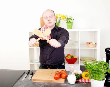 Fun image of a man preparing to start cooking a healthy vegetarian meal standing holding up the wooden salad utensils crossed in front of him with a look of determination