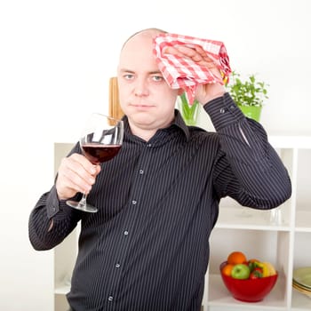 Man wiping his brow with a dishcloth as he takes a break from the frustration of cooking to enjoy a glass of red wine