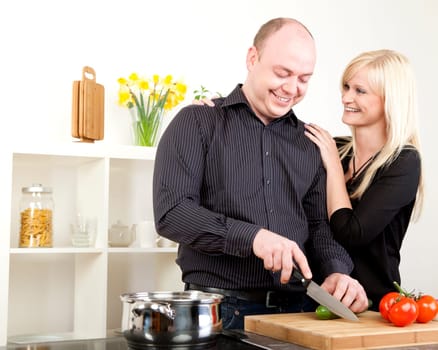 Affectionate couple standing together with the wife caressing her husband as he stands chopping vegetables and preparing dinner in the kitchen