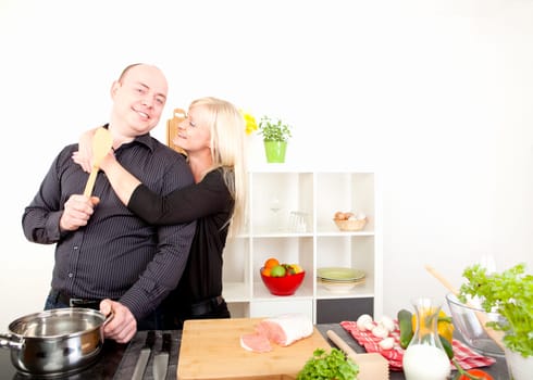 Romantic happy couple enjoying an affectionate embrace stand in the kitchen preparing a meal from an array of fresh healthy ingredients