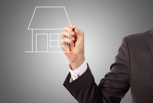 Male hand drawing a house on glass board, grey background