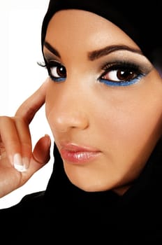 A pretty and young teen girl with a black headscarf and nice makeup looking into the camera with one finger on her face for white background.