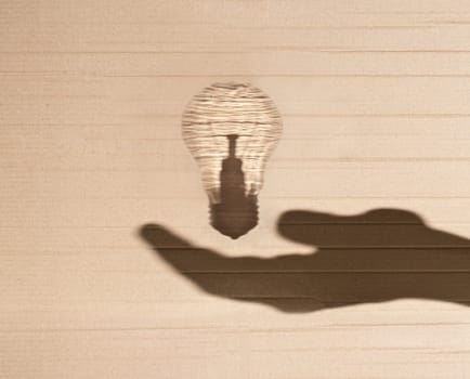 shadow of human hand holding shadow of light bulb against cardboard background
