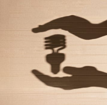 shadow of human hands holding shadow of fluorescent light bulb against cardboard background