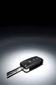 Modern black open car key on dark background in spot of light, wide angle, horizontal.