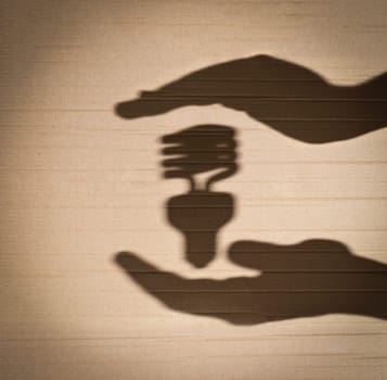 shadow of human hands holding shadow of fluorescent light bulb against cardboard background