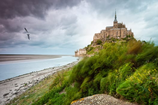 View of Mont Saint-Michel at windy day. Dark stormy clouds in background (Saint Michael's Mount, Normandy, France, Europe).