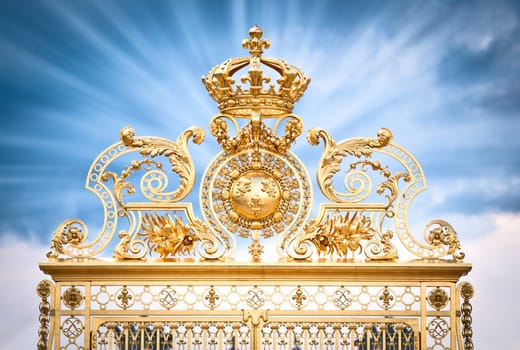 Golden ornate gate of Chateau de Versailles with blue sky, with clouds background. Rays of light from gate. Paris, France, Europe.
