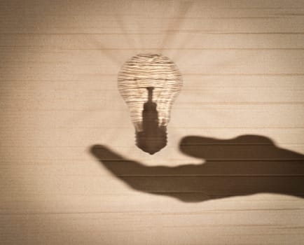 shadow of human hand holding shadow of light bulb against cardboard background