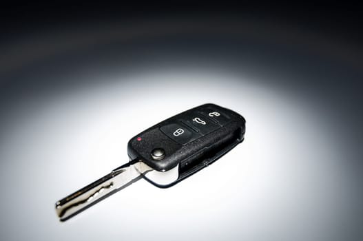 Modern black open car key on dark background in spot of light, wide angle, horizontal.
