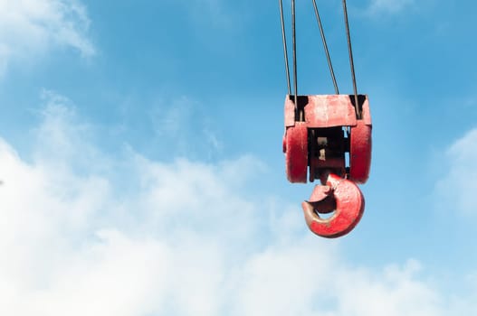 red old crane hook with blue cloudy sky in background.