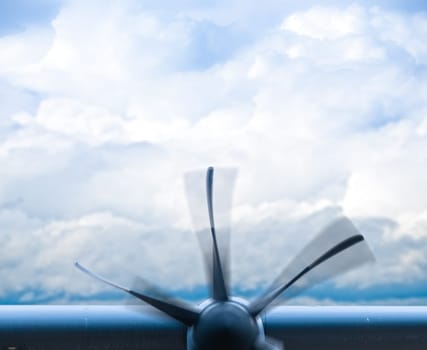 Plane engine with rotating propeller with motion blur. Blue cloudy sky in background.