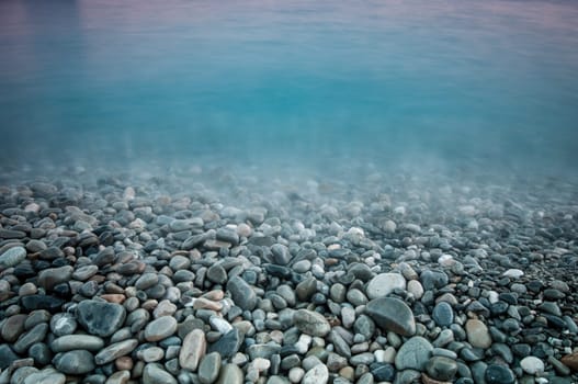 pebble stones by the sea. Silky waves of blue sea from long exposure.