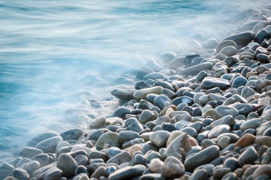 pebble stones by the sea. Silky waves of blue sea from long exposure.