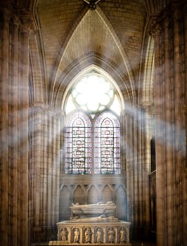 sun rays beaming through the old stained glass window of saint denis cathedral and lighting interior with tomb. Paris, France, Europe.