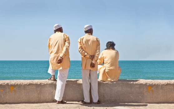 Horizontal portrait of three clerics in formal attire looking  out to the horizon of the Arabian Sea. The location of this conceptual shot was at the beach and promenade at Dwarka, Gujarat, India near the Krishna Temple.