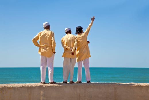 Horizontal portrait of three clerics in formal attire looking and pointing out to the horizon of the Arabian Sea. The location of this conceptual shot was at the beach of Dwarka Bay, Gujarat, India near the Krishna Temple.