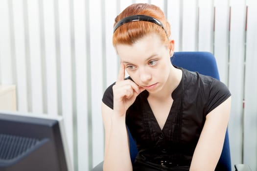 Worried despondent businesswoman sitting morosely at her desk staring at the monitor of her desktop computer