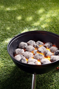 High angle view of glowing hot charcoal coals in a small portable barbecue standing on grass in preparation for cooking a healthy outdoor meal