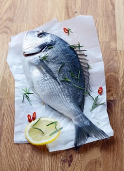 Whole fresh fish lying with the tail towards the camera on a sheet of crumpled paper on a wooden tabletop waiting to be cleaned and filleted for cooking