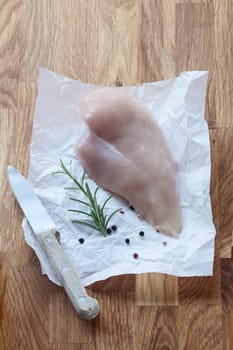 Fresh uncooked fish fillet with rosemary lying on a sheet of crumpled paper on a wooden kitchen table