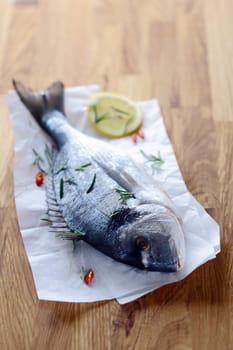 Whole raw fish on crumpled paper lying on a wooden kitchen table waiting to be filleted to cook as an enjoyable seafood dinner
