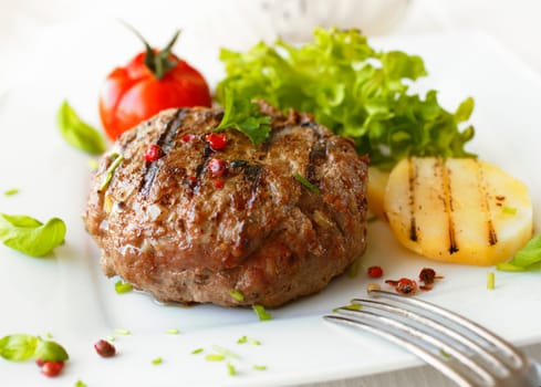 Delicious grilled beef meatball served on a white plate with tomato and lettuce with a fork in the foreground