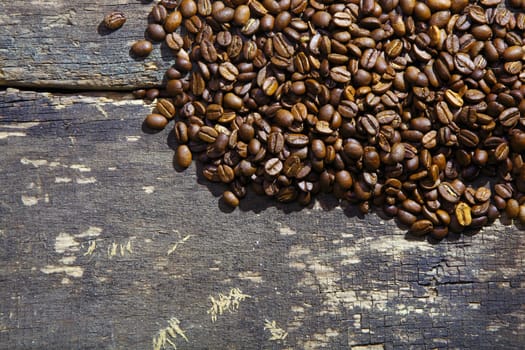 Pile of rich brown freshly roasted aromatic coffee beans on an old grunge wooden surface with copyspace