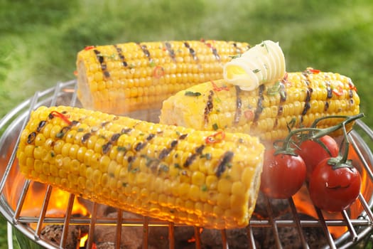 Healthy vegetarian barbecue with ripe golden corn on the cob and juicy red cherry tomatoes grilling over the fire outdoors on a green lawn
