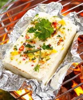 High angle view of a portion of feta or halloumi cheese topped with seasoning and spices grilling on a barbecue