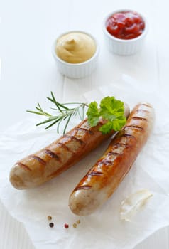 Two succulent sausages with herbs and sauces on a white plate.