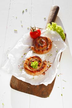 Rolled sausage with tomato on the wooden plate