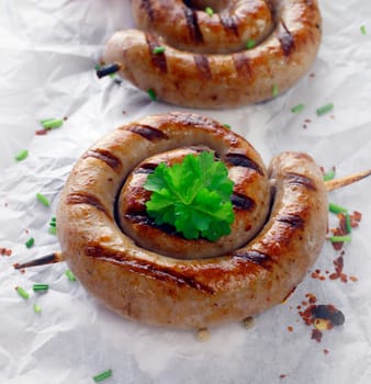 Close up of a cooked sausage in a swirl shape with a wooden skewer and a sprig of parsley.
