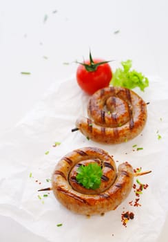 Rolled Bratwurst with tomato on stick over the white background