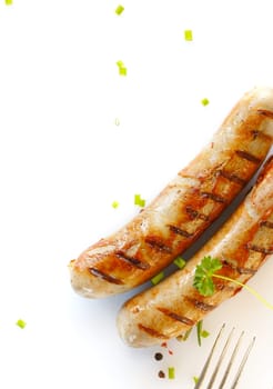 Two cooked sausages side by side against showing prongs of a fork against a white background.