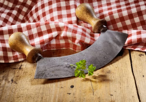Modern herb cutter (wiegemes) with wooden handles with a sprig of parsley against a red gingham cloth.