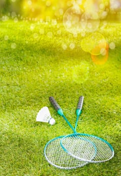 Badminton rackets and shuttlecock lying on a lush green lawn in warm golden summer sunlight with flare and bokeh