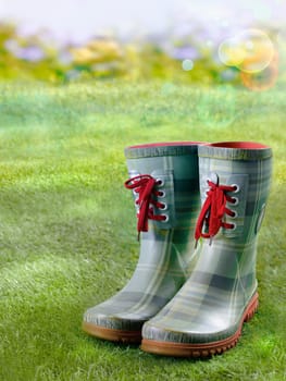 Pair of stylish green boots with red laces standing on a green lawn in a sunbeam with golden bokeh
