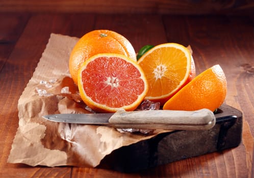 Juicy oranges, one whole and some sliced in halves on brown paper with knife