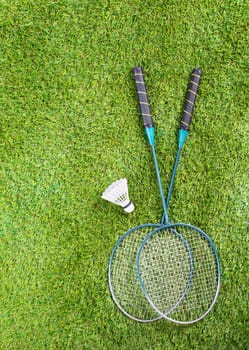 Overhead view of a pair of badminton racquets and a shuttlecock lying on a green lawn with copyspace
