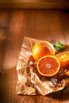 Two juicy oranges, one sliced in halves on brown paper