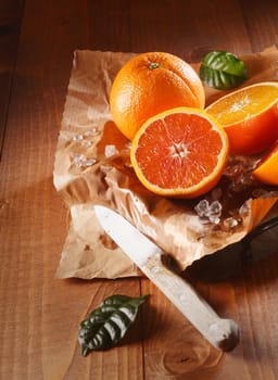 Two juicy oranges, one sliced in halves on brown paper and knife