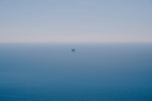 Yacht with three sails floats on the blue sea on the horizon. High quality photo