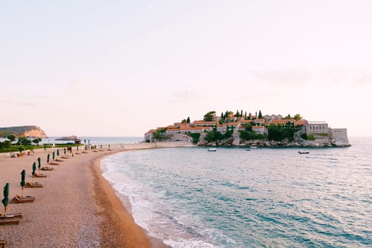 Sandy spit with sun loungers near the isthmus of the island of Sveti Stefan. Montenegro. High quality photo