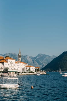Boats are moored in the sea off the coast of Perast with old houses and a church bell tower. Montenegro. High quality photo