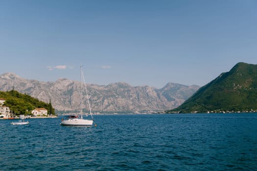 Sailing yacht is moored in the sea near the shore of an old town at the foot of the mountains. High quality photo