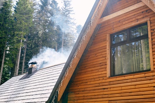 Smoke rises from a chimney on the roof of a wooden house in the forest. High quality photo