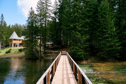 Wooden bridge across the lake to a house on the shore in a spruce forest. High quality photo