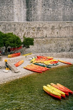 Colorful kayaks dry on the shore next to the oars near the fortress wall. High quality photo
